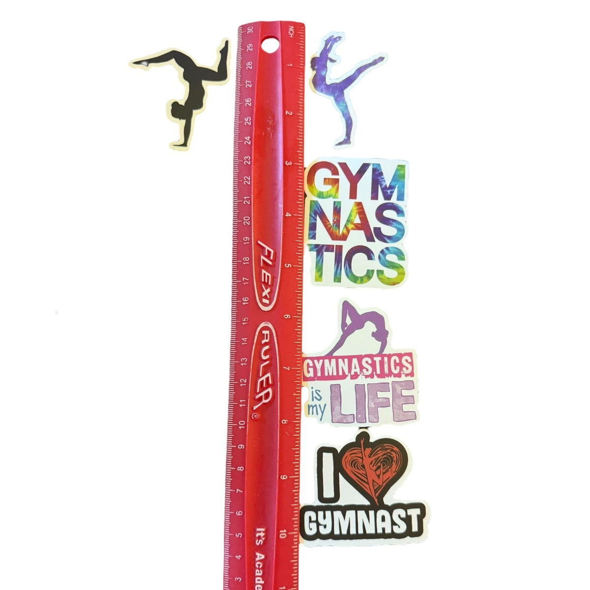 A set of gymnastics-themed stickers displayed next to a red ruler for scale on a white background. The stickers include silhouettes of gymnasts in different poses, the word 'GYMNASTICS' in a rainbow gradient, 'GYMNASTICS is my LIFE' with a pink heart.