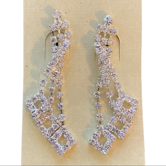 A pair of silver-tone drop earrings covered in clear rhinestones, displayed on a beige card against a white background.
