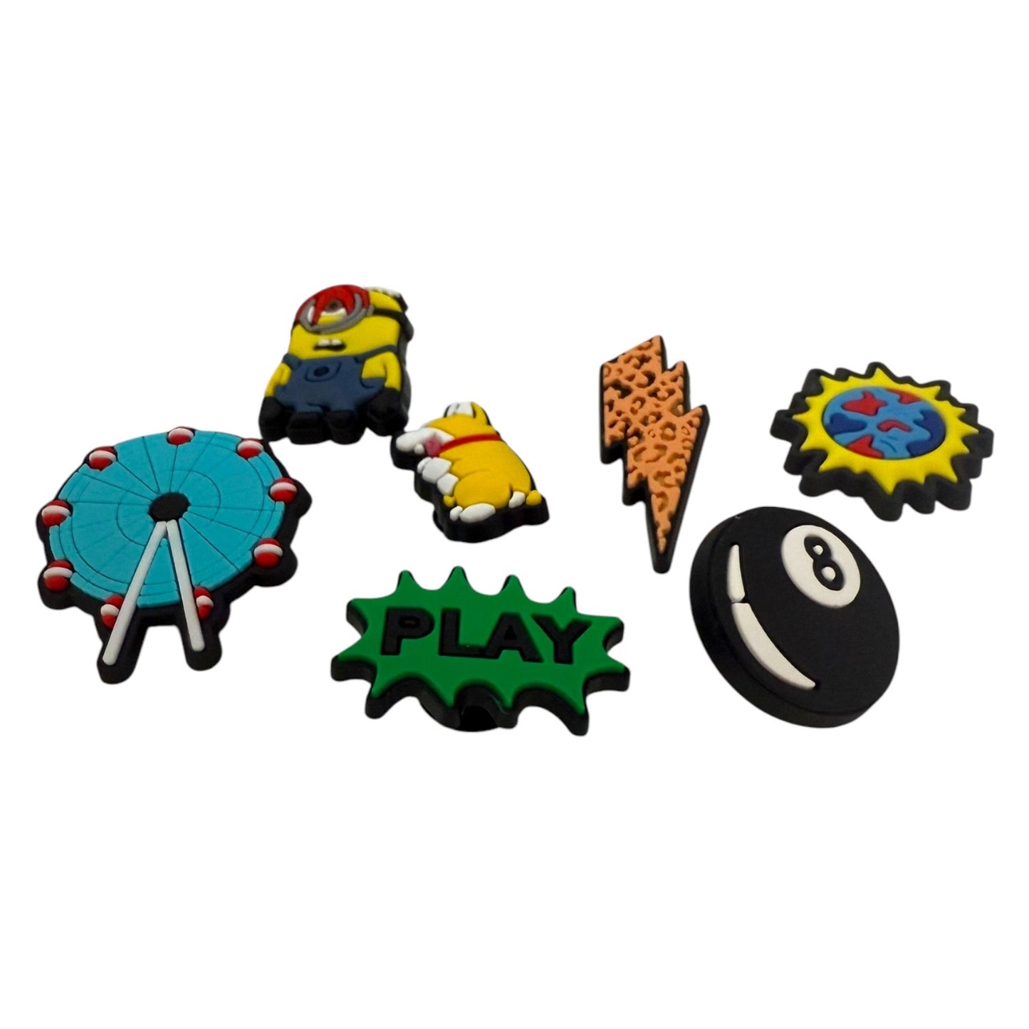 Six colorful novelty shoe charms arranged on a plain white background, including a Ferris wheel, a yellow cartoon character, a green 'PLAY' burst, a lightning bolt, a sun, and a black-and-white 8-ball.