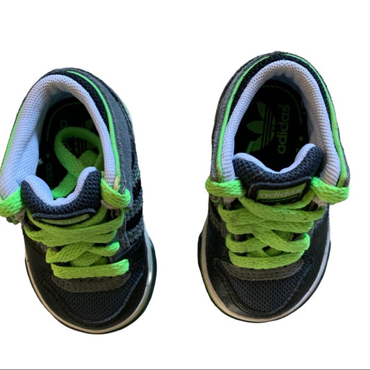 A pair of Adidas toddler sneakers shown from the front on a white background. The shoes are dark gray with bright neon green laces and trim.