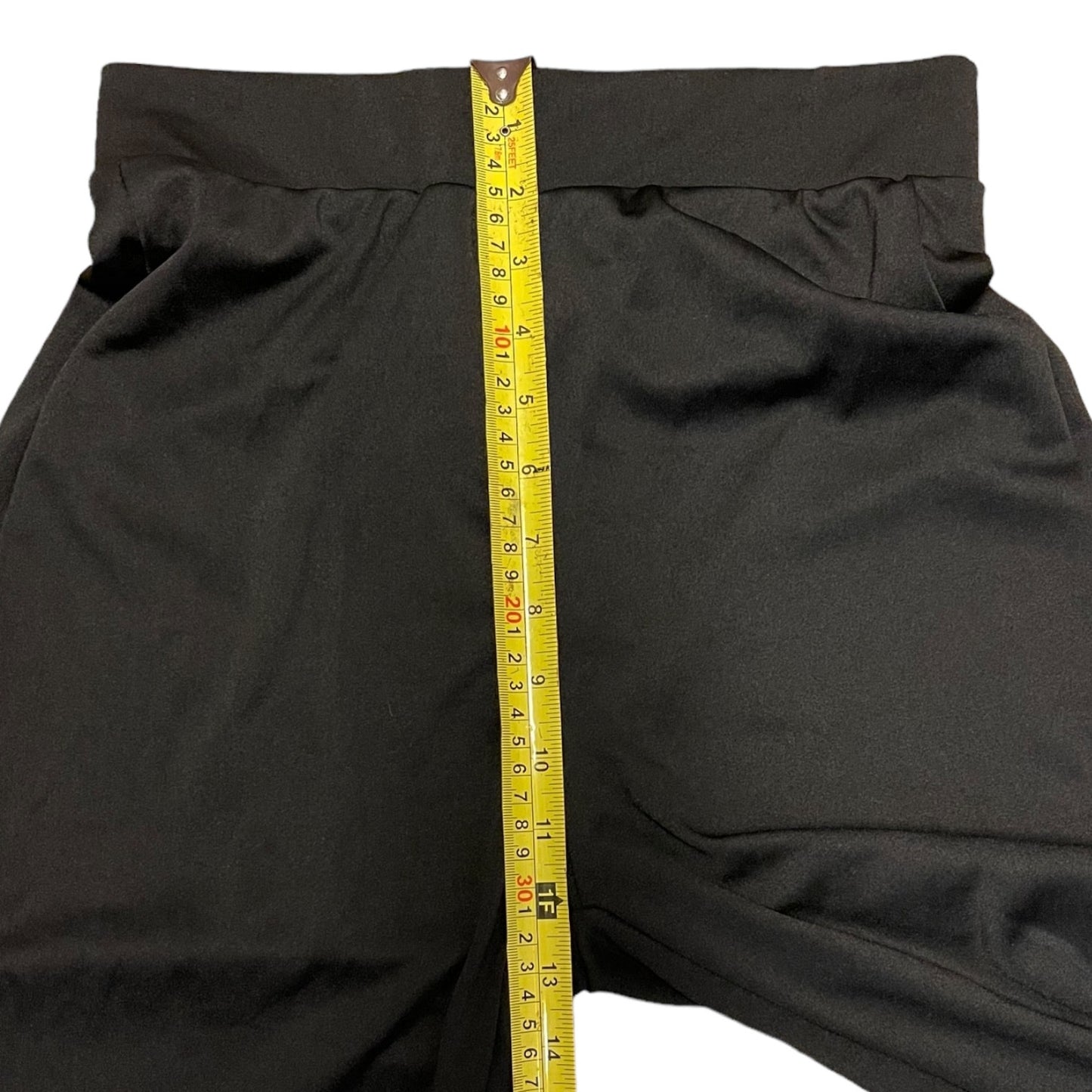 Black pants with a yellow measuring tape vertically aligned down the center to show the waistband measurement.