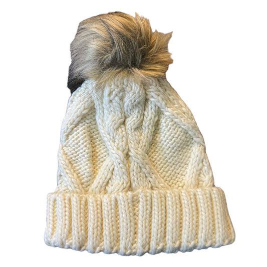Cream cable-knit beanie hat with a ribbed cuff and a fluffy brown and cream pom-pom on top, shown against a plain white background.