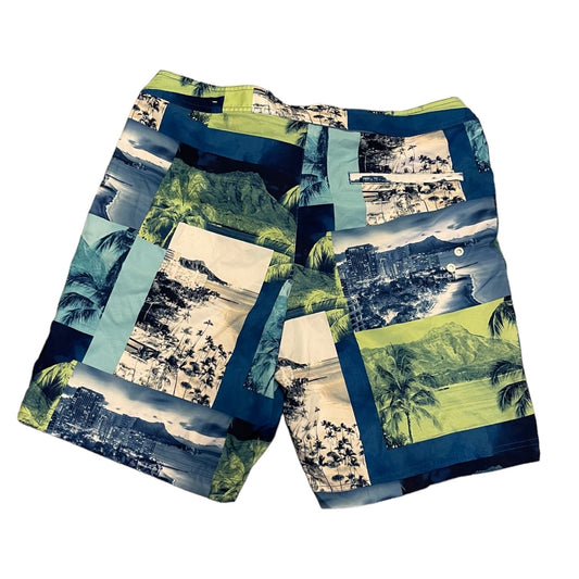 A pair of men's swim trunks featuring a patchwork collage print of tropical beach scenes, palm trees, and coastal landscapes in shades of blue, green, beige, and black.