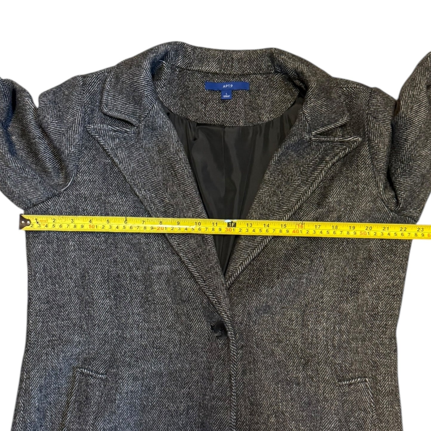 A gray jacket laid flat on a white background, with a yellow tape measure stretched horizontally across the chest to show the width.