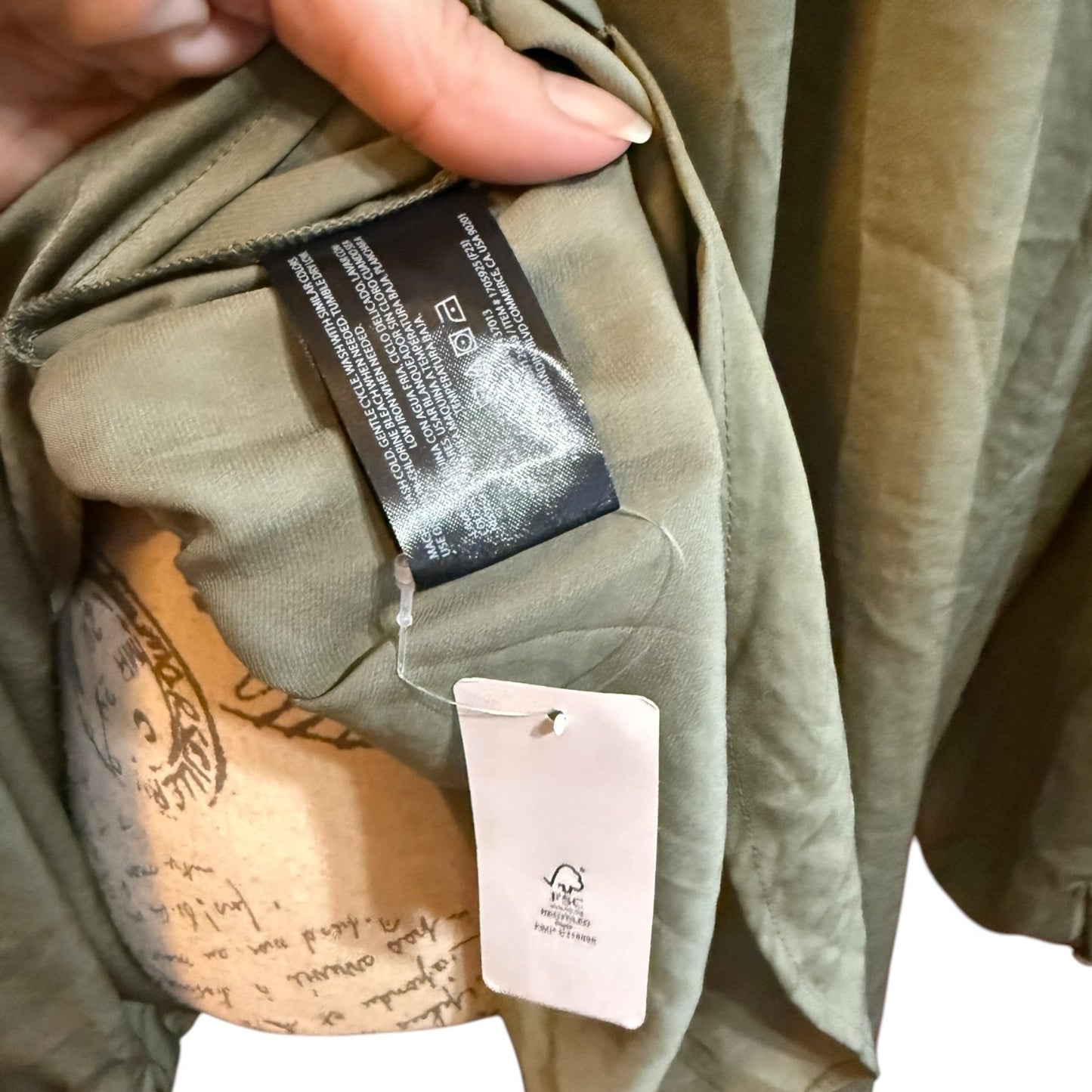 Close-up of a garment being held open by a hand, showing an olive green fabric interior with a black care label and a white material tag.