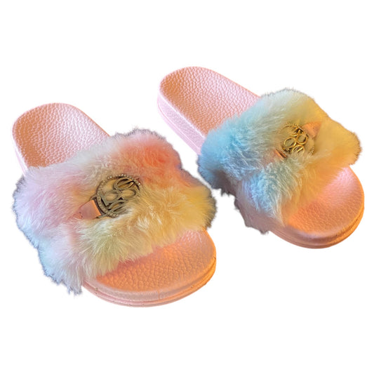 A pair of pastel slide sandals with fluffy faux-fur straps in a soft rainbow gradient and a silver-tone circular metal emblem on the top, shown on a plain white background.