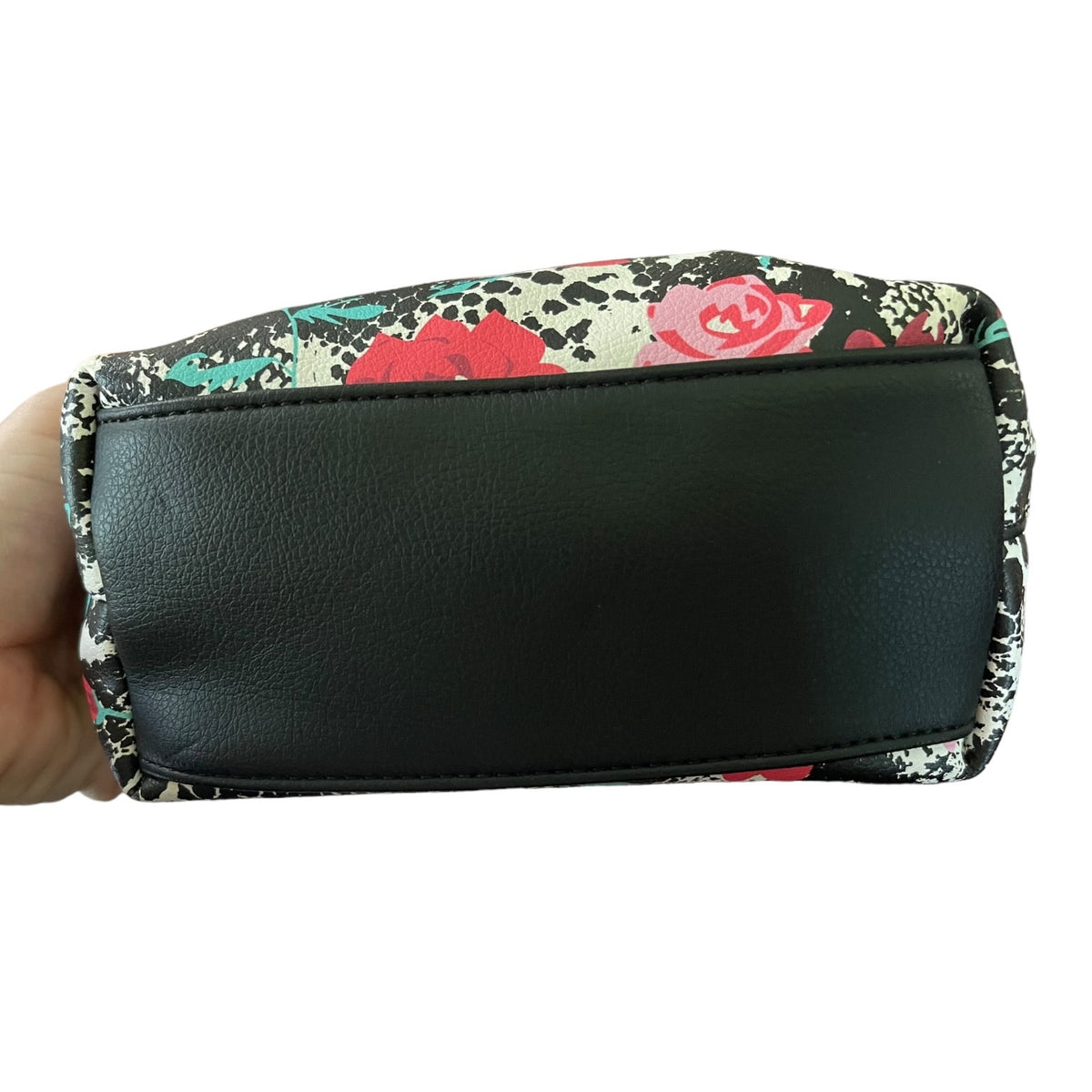 A hand holding a floral purse showing the bottom as black on a white background.