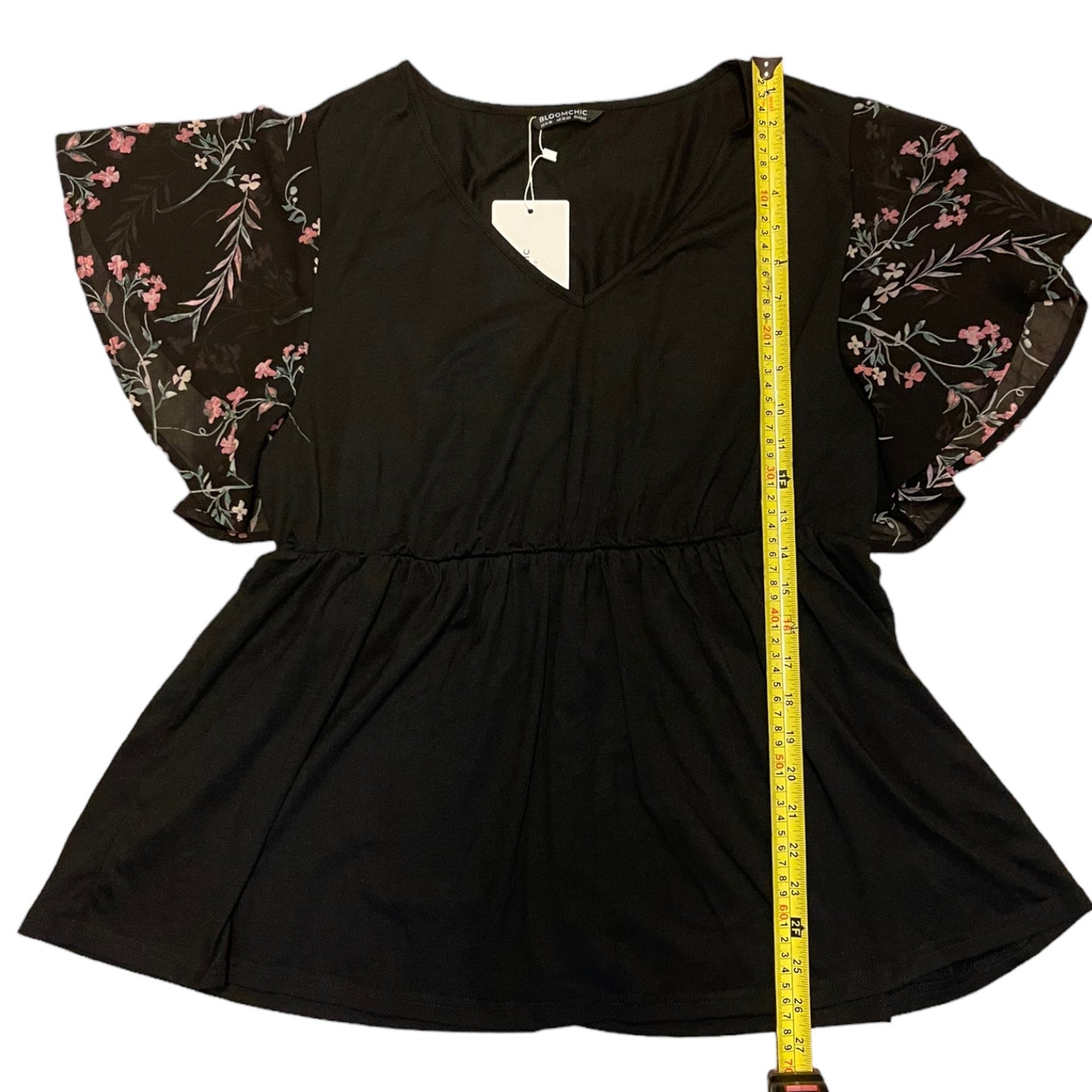 Black shirt with floral sleeves and a measuring tape for size reference on a white background