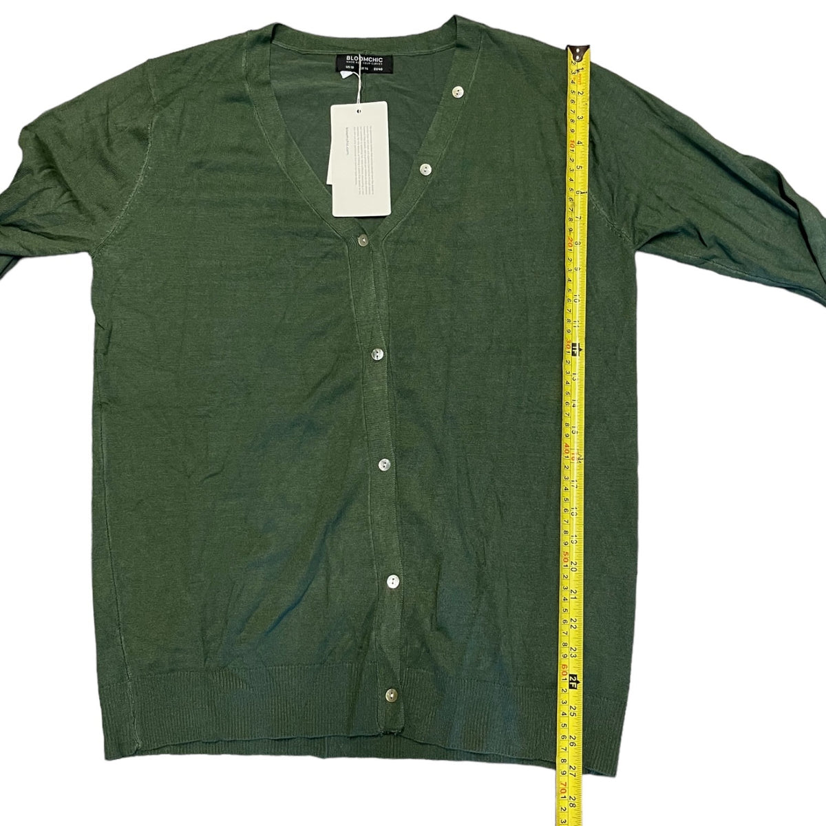 An green long-sleeve button-up cardigan sweater laid flat on a white background, with a yellow tape measure standing vertically next to it for size reference.