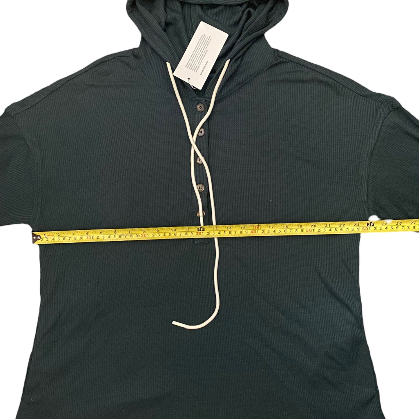 Dark green hoodie with a measuring tape draped over it on a white background