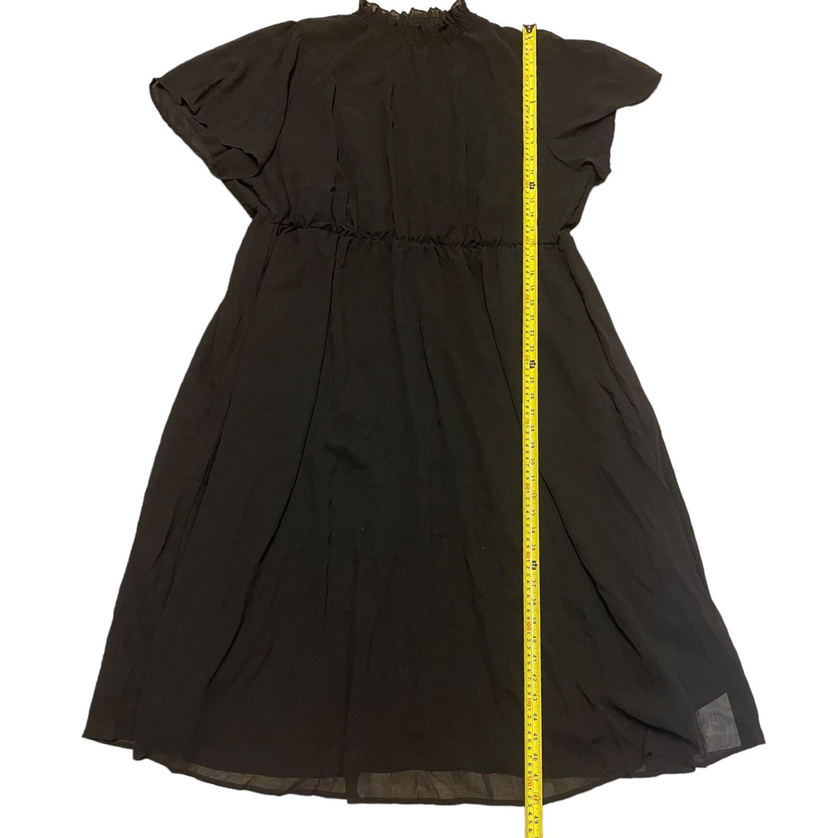 A black dress with flutter sleeves and a gathered waist, shown flat against a white background with a yellow measuring tape running vertically to indicate height.