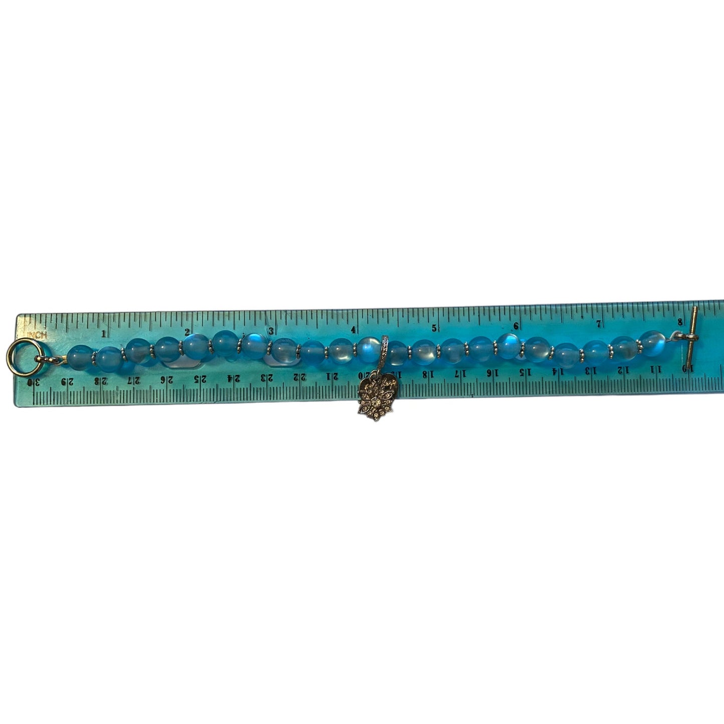 Blue beaded bracelet with a silver charms on a ruler for size reference