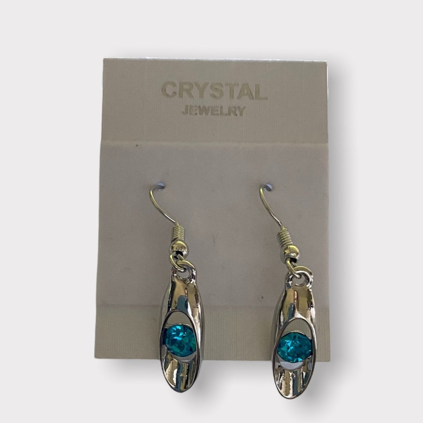 A pair of dangling earrings with silver-toned metal frames and round blue- crystal centers, displayed on a jewelry card labeled 'CRYSTAL JEWELRY'.