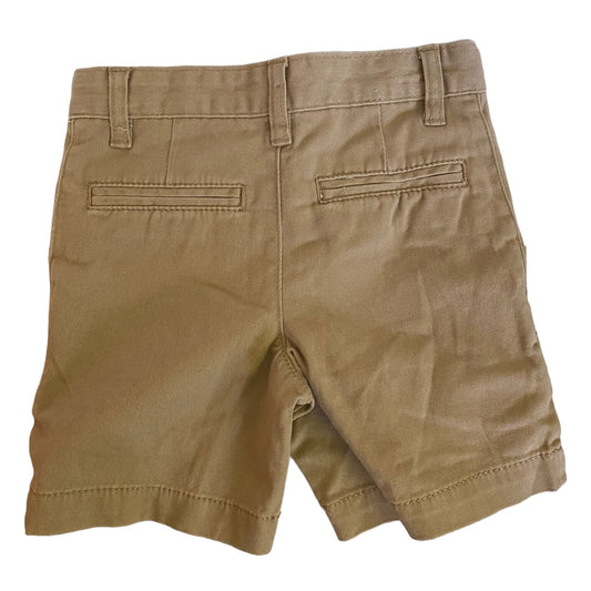 A pair of beige-colored chino shorts shown from the back, featuring belt loops, a central seam, and two welt back pockets, laid flat against a white background.