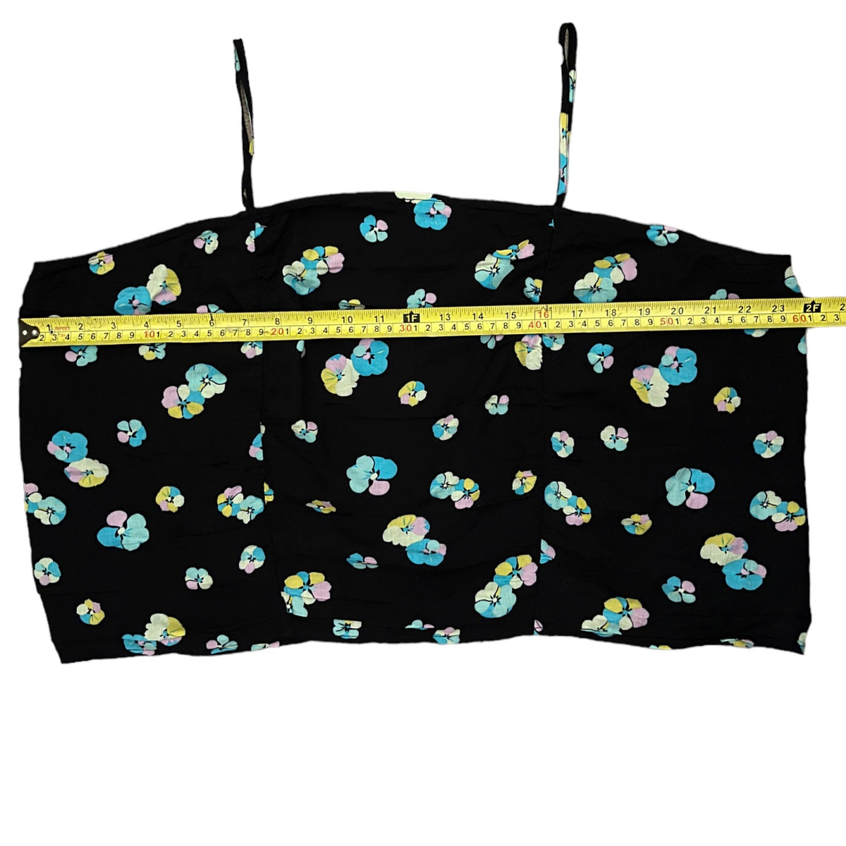 A black spaghetti-strap crop top with a colorful floral pattern, shown with a yellow tape measure across the chest to indicate size.