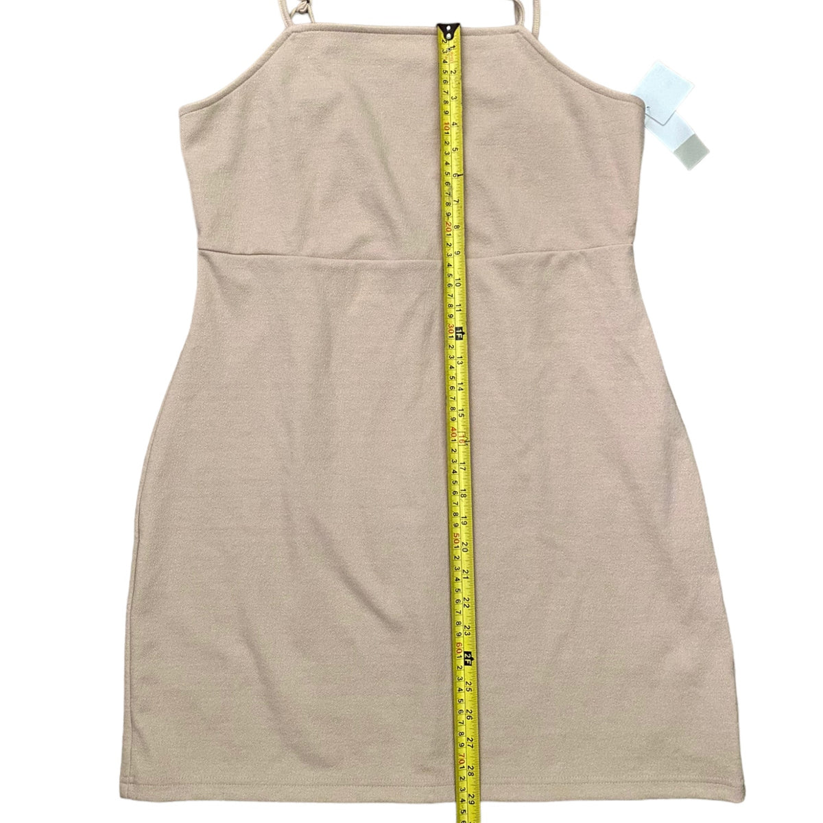 A beige sleeveless dress shown flat against a white background, with a yellow measuring tape vertically aligned down the center to indicate its height. A small light blue tag is visible near the shoulder.
