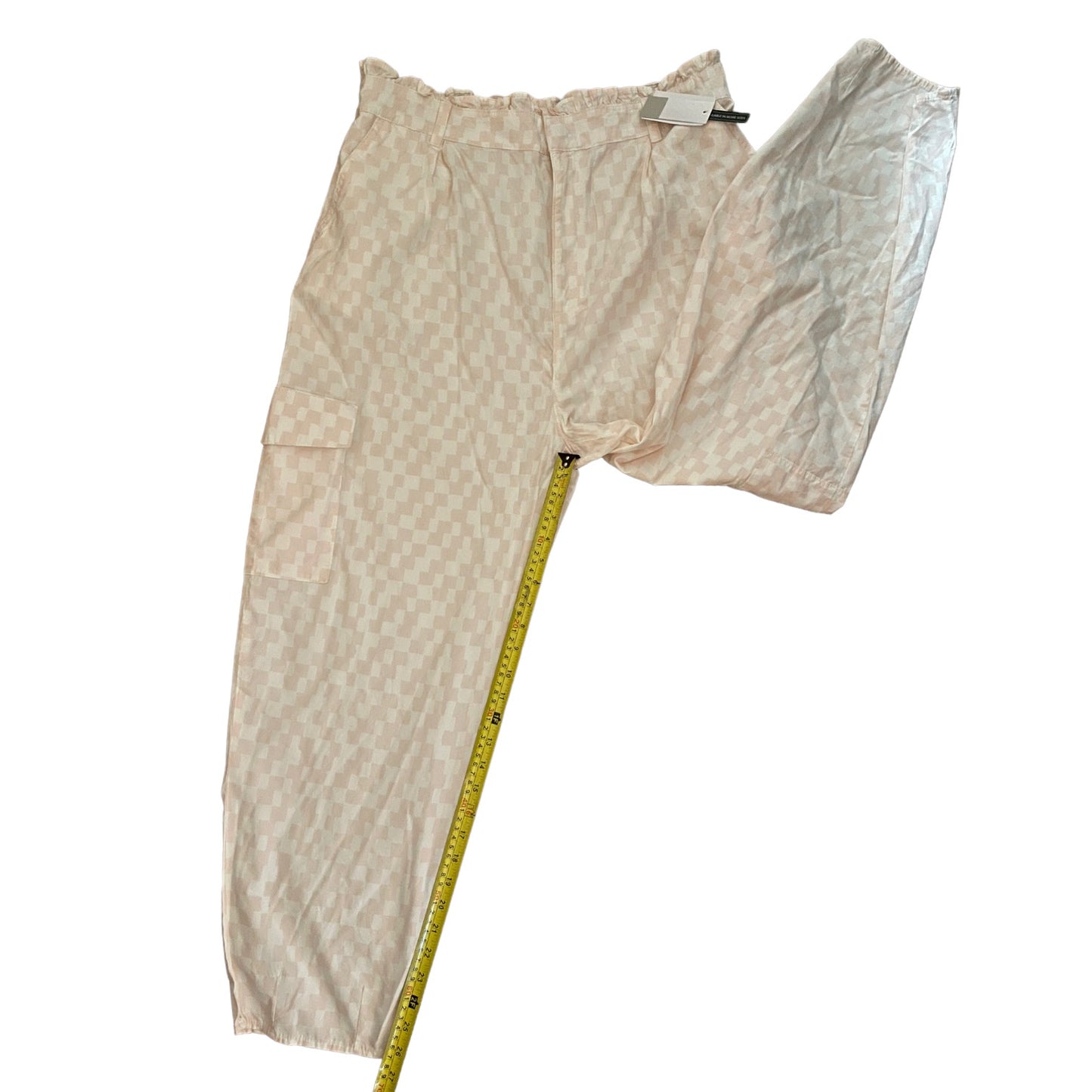 Pink and white checkered pants with a yellow measuring tape measuring inseam on a white background