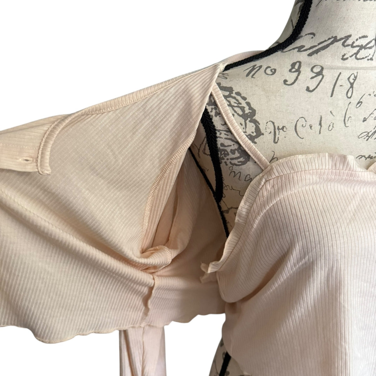 A close-up of a light beige ribbed knit cardigan and tank displayed on a vintage-style dress form mannequin against a white background.