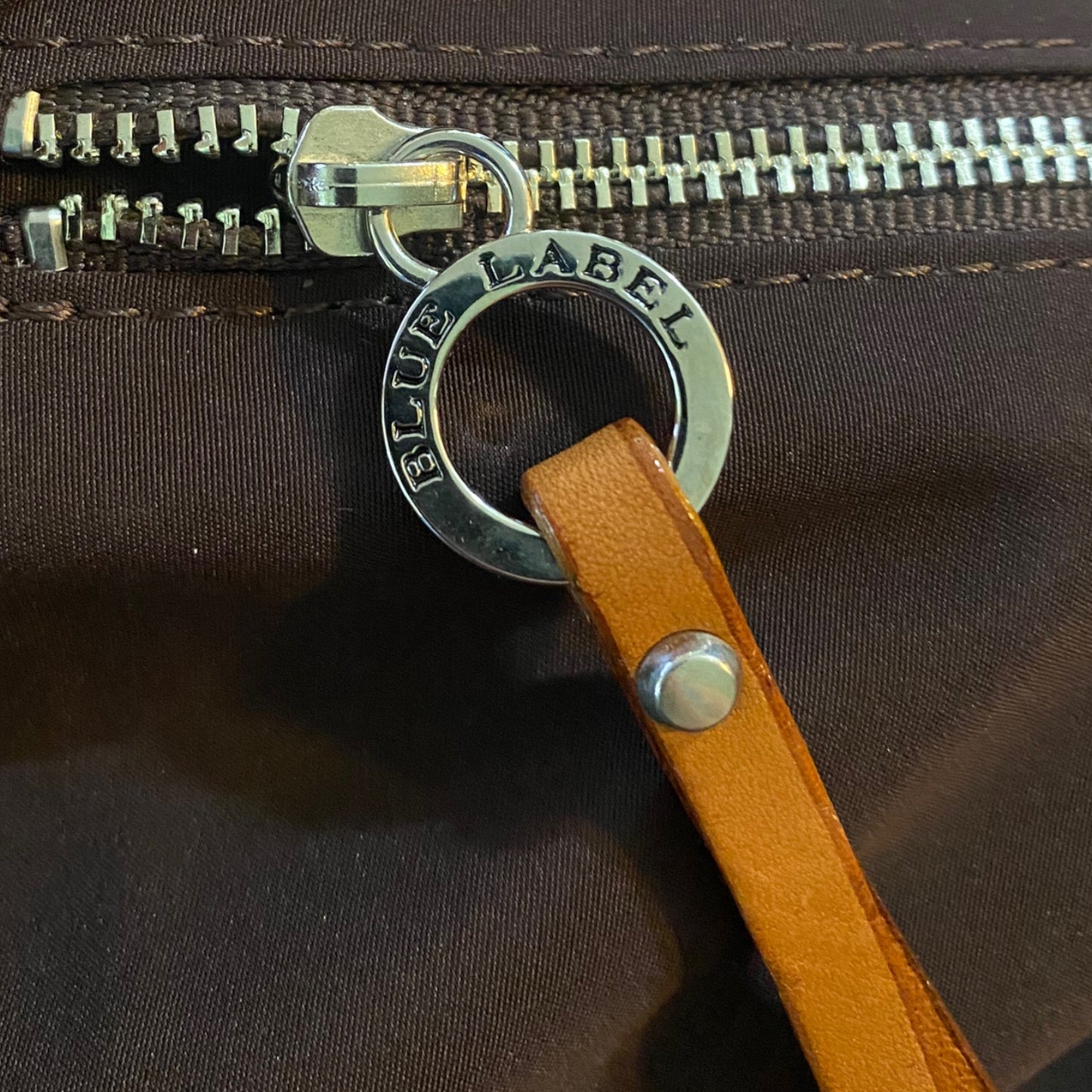 Close-up of a brown interior of bag with a leather strap and 'Blue Label' zipper pull.