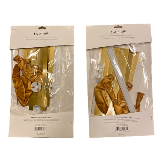 Two packaged sets of gold and white balloon garlands and matching ribbon rolls on a plain white background. The packages are labeled 'Cakesalk'.