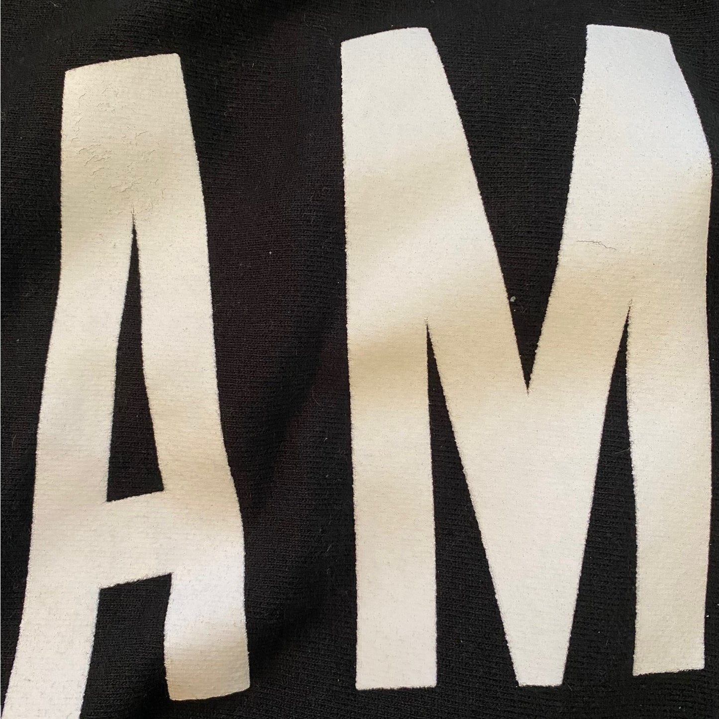 Close-up of a black fabric with large, white, embroidered letters spelling 'AM'.