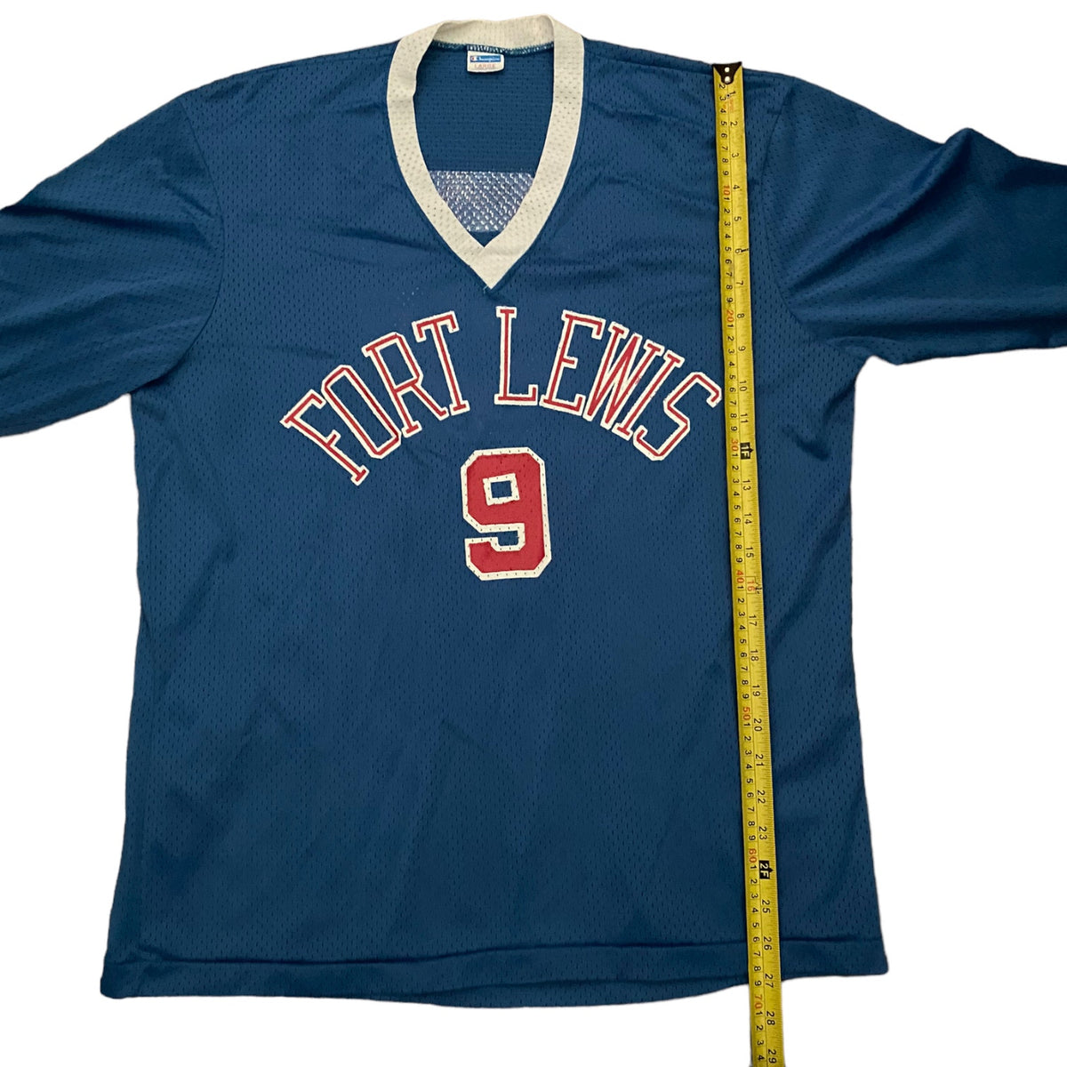 Blue Fort Lewis shirt with a 9 on front laying down flat with a yellow measuring tape