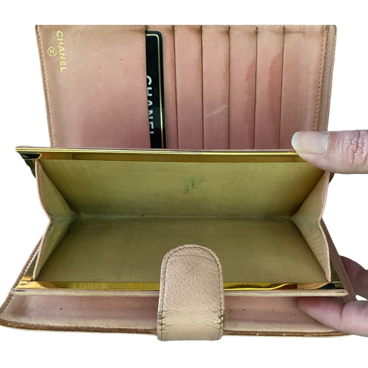 A Chanel wallet in light pink leather, shown open with a hand holding it. The interior features a gold-tone coin pocket with beige interior