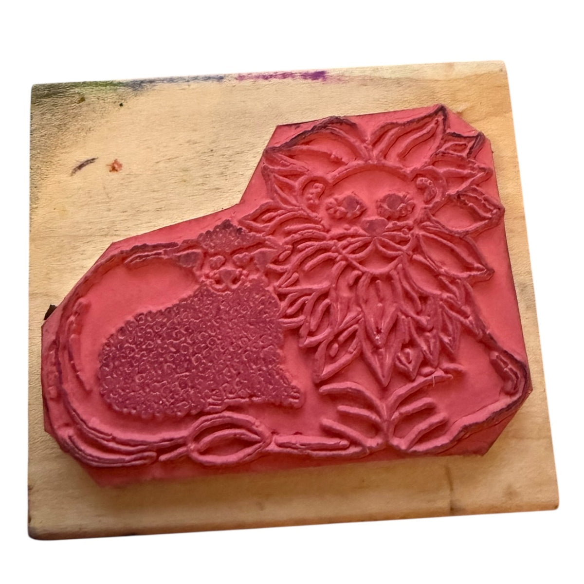 A red rubber stamp featuring a carved lion and lamb, displayed on a light-colored wooden block against a white background.