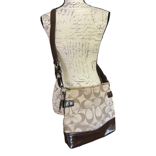 A Coach crossbody bag with a beige and brown signature 'C' monogram pattern and dark brown patent leather trim, displayed on a cream-colored mannequin torso against a white background.