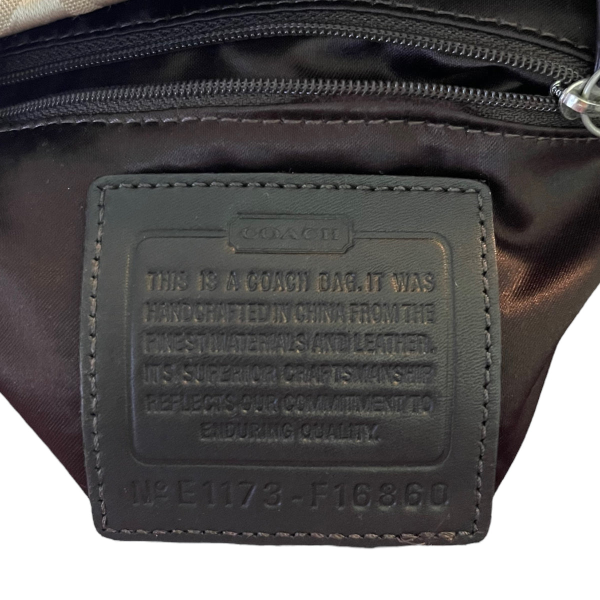 Close-up of a Coach bag showing a brown leather embossed brand patch with product details.