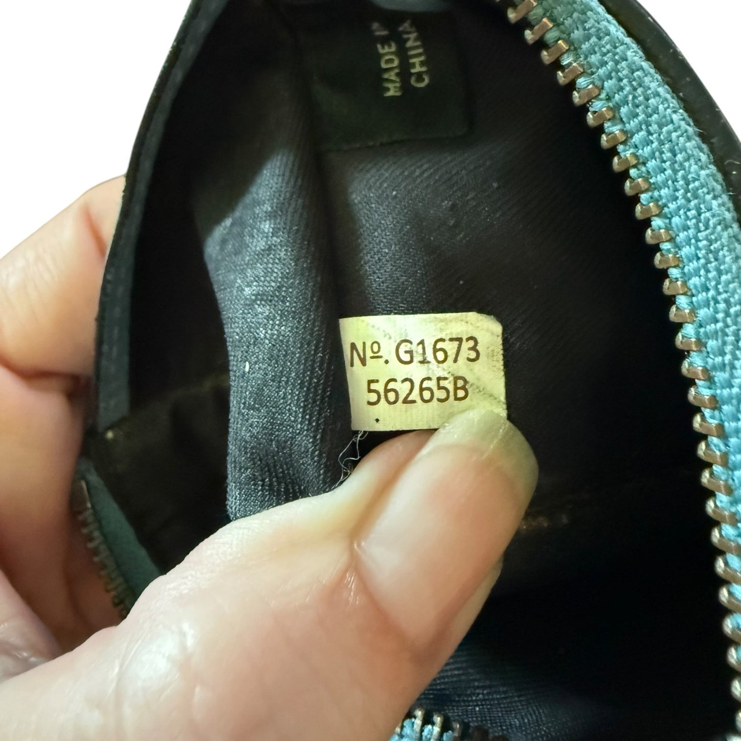 Hand holding a blue leather wallet with a visible gold tag and 'Made in China' label.