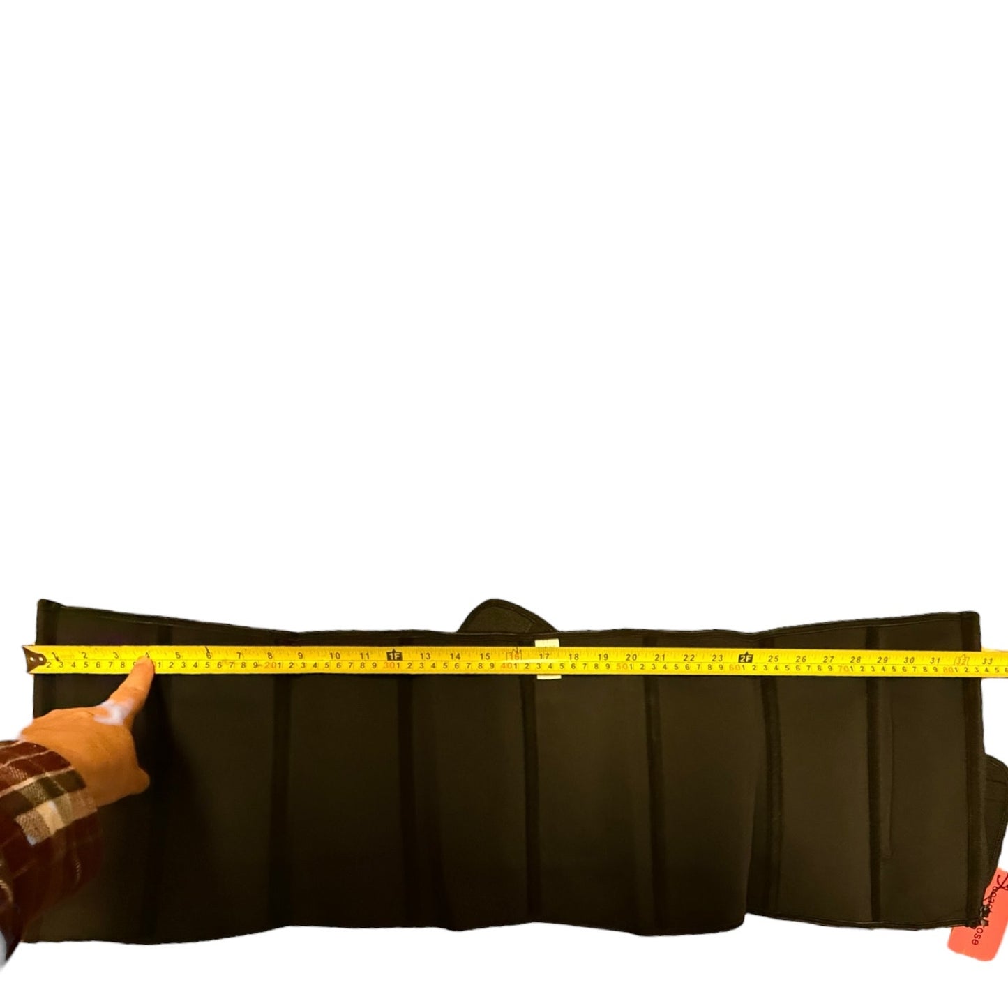 A black wait trainer laying out unfolded being measured horizontally with a yellow tape measure, with a hand pointing at the measurement on the left.