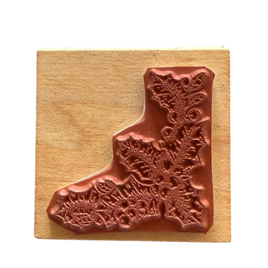 A holly and berries rubber stamp, mounted on a square light wood block against a plain white background.