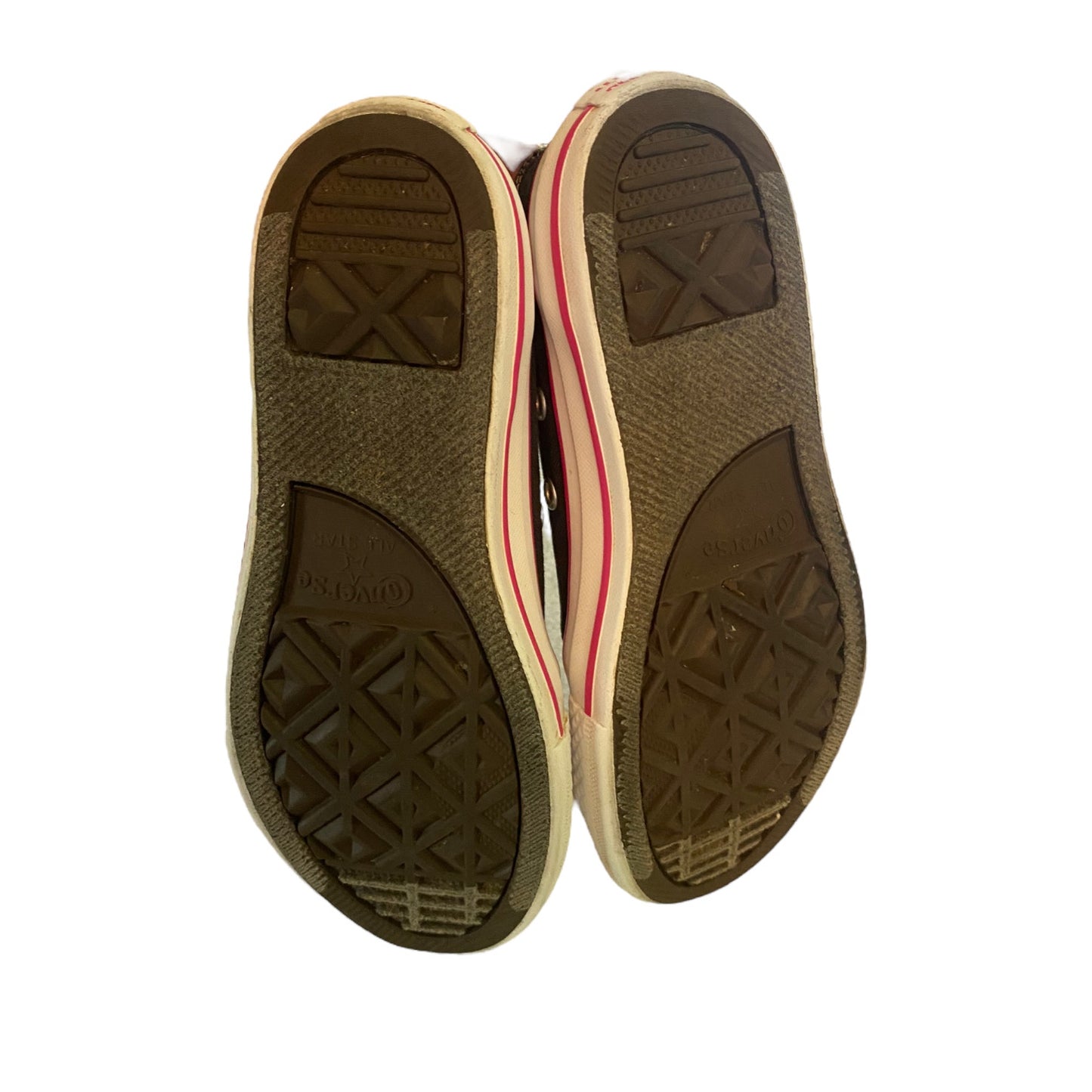 The soles of a pair of Converse-style shoes, showing the dark brown textured rubber outsoles with the Converse 'X' logo and 'MADE IN THE USA' embossed, with a beige midsole and a thin red stripe visible on the sides.