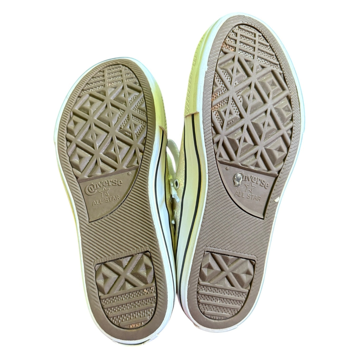 Top-down view of a pair of Converse All Star sneakers showing the textured brown rubber soles against a white background.