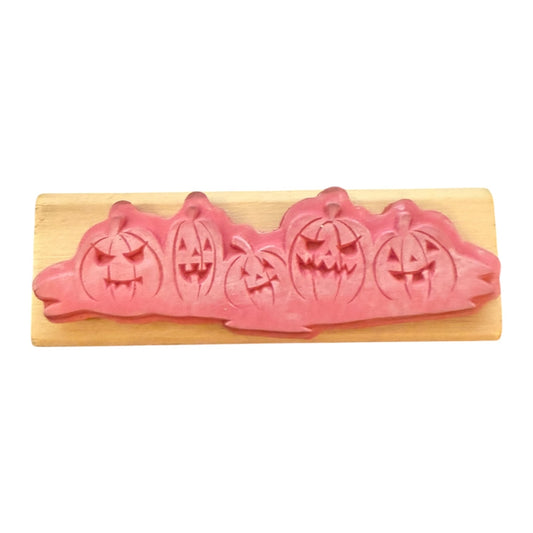 Pink pumpkin-shaped rubber stamp on a wooden board with a white background
