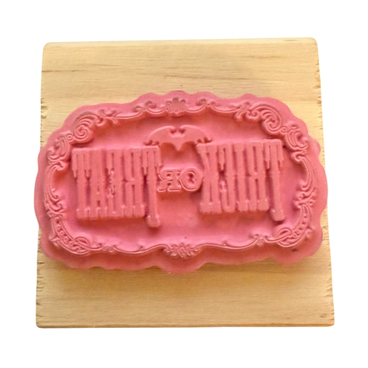 A pink rubber stamp featuring a design with a bat and the words 'Trick or Treat,' displayed on a light wood block against a white background.