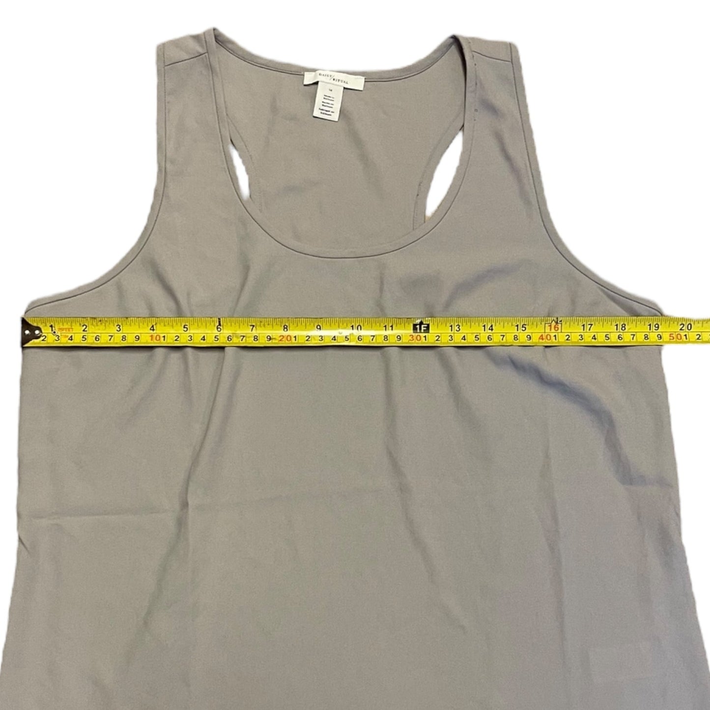 A light gray racerback tank top laid flat on a white background with a yellow tape measure stretched horizontally across the chest to show the width.