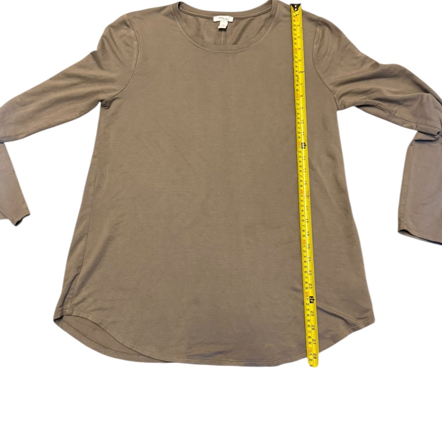A light mocha long-sleeve tunic top laid flat on a white background, with a yellow tape measure standing vertically along the right side to show the garment's height.