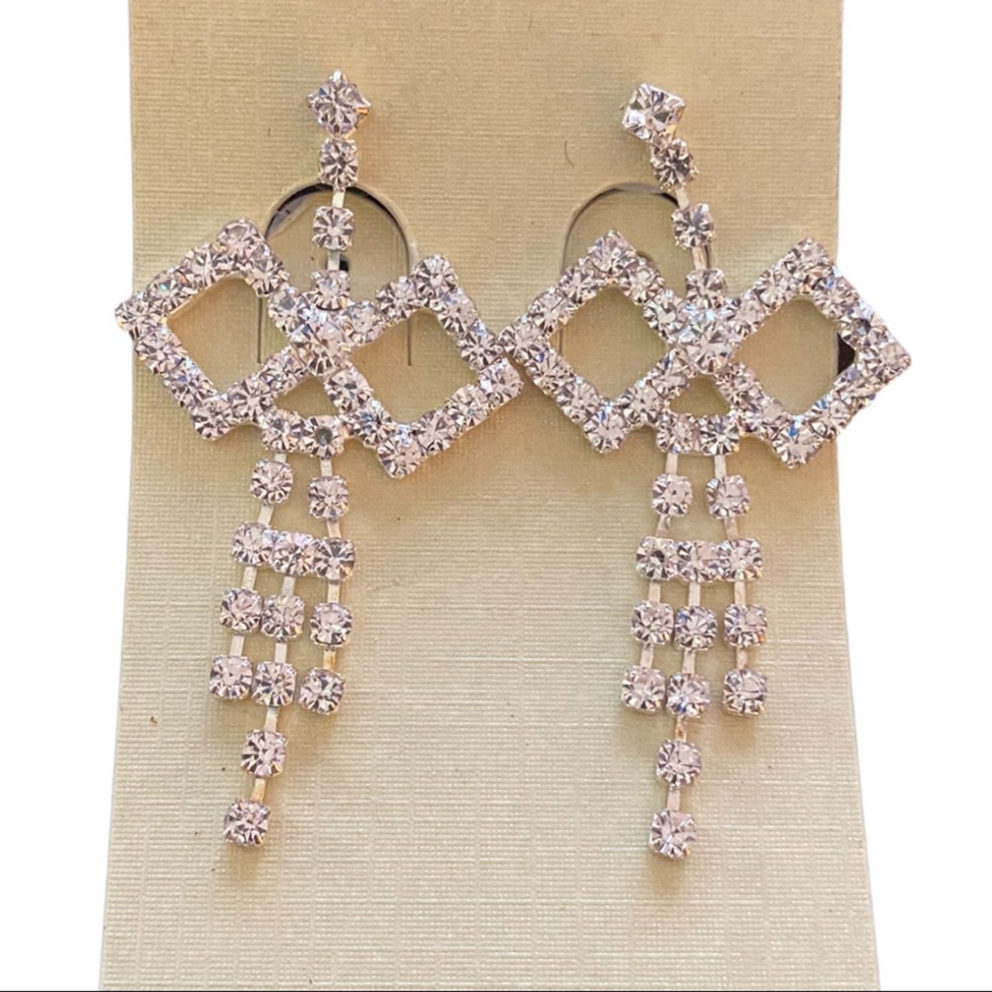 Pair of diamond-shaped earrings with dangling crystals on a beige card.