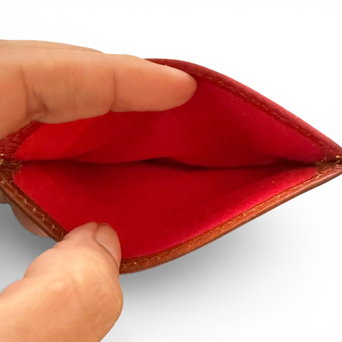 Hand holding an open leather wallet with a red interior on a white background