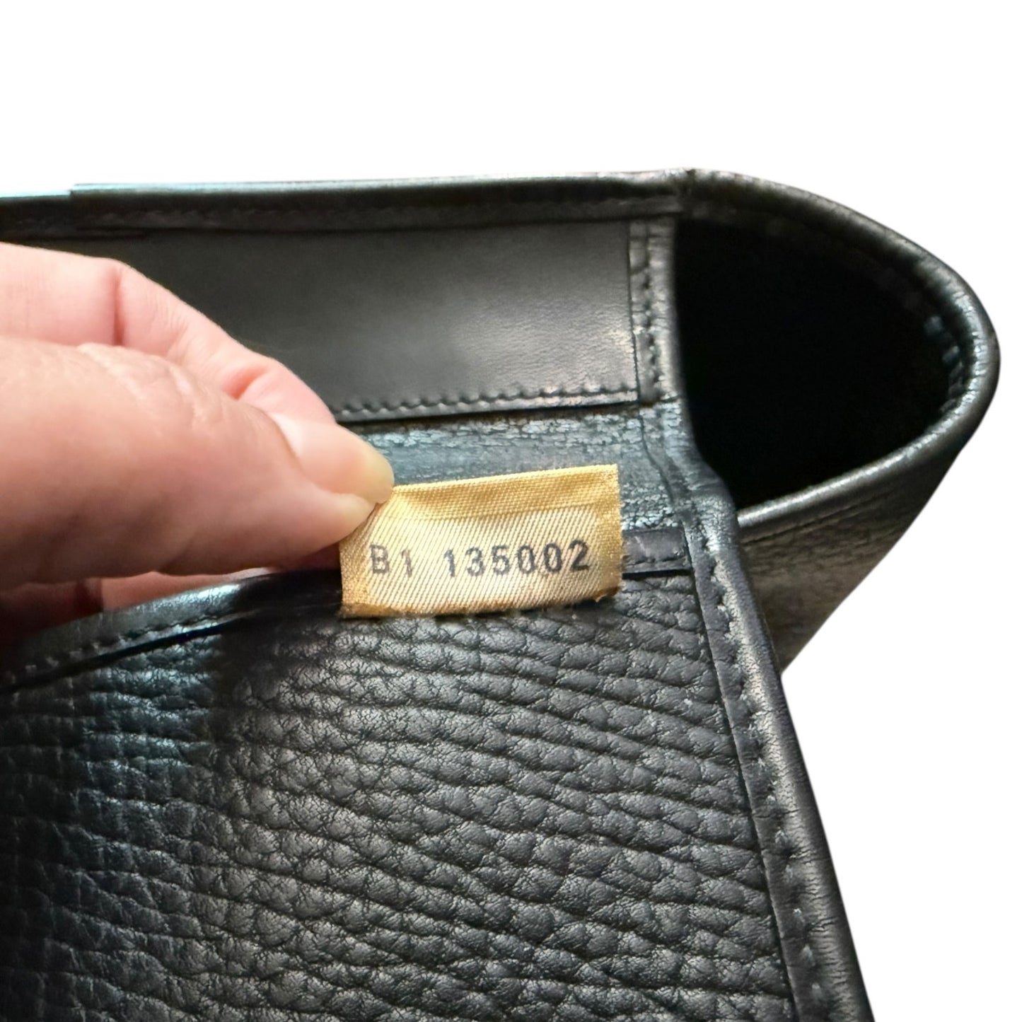 Close-up of a black leather product with a visible tag, held by a hand.