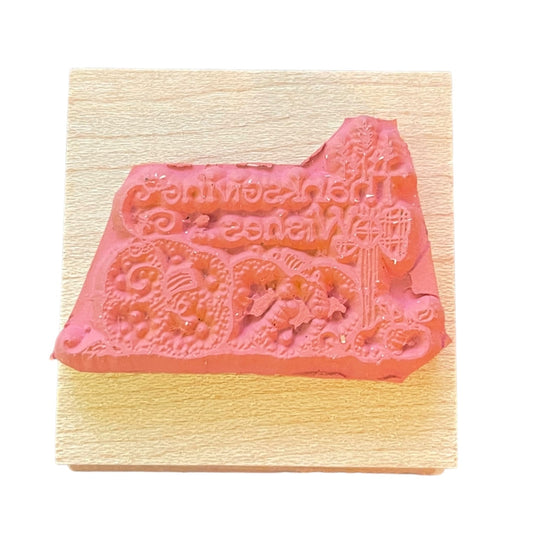 A pink stamp with a decorative holiday and script design, mounted on a light wood block against a white background.