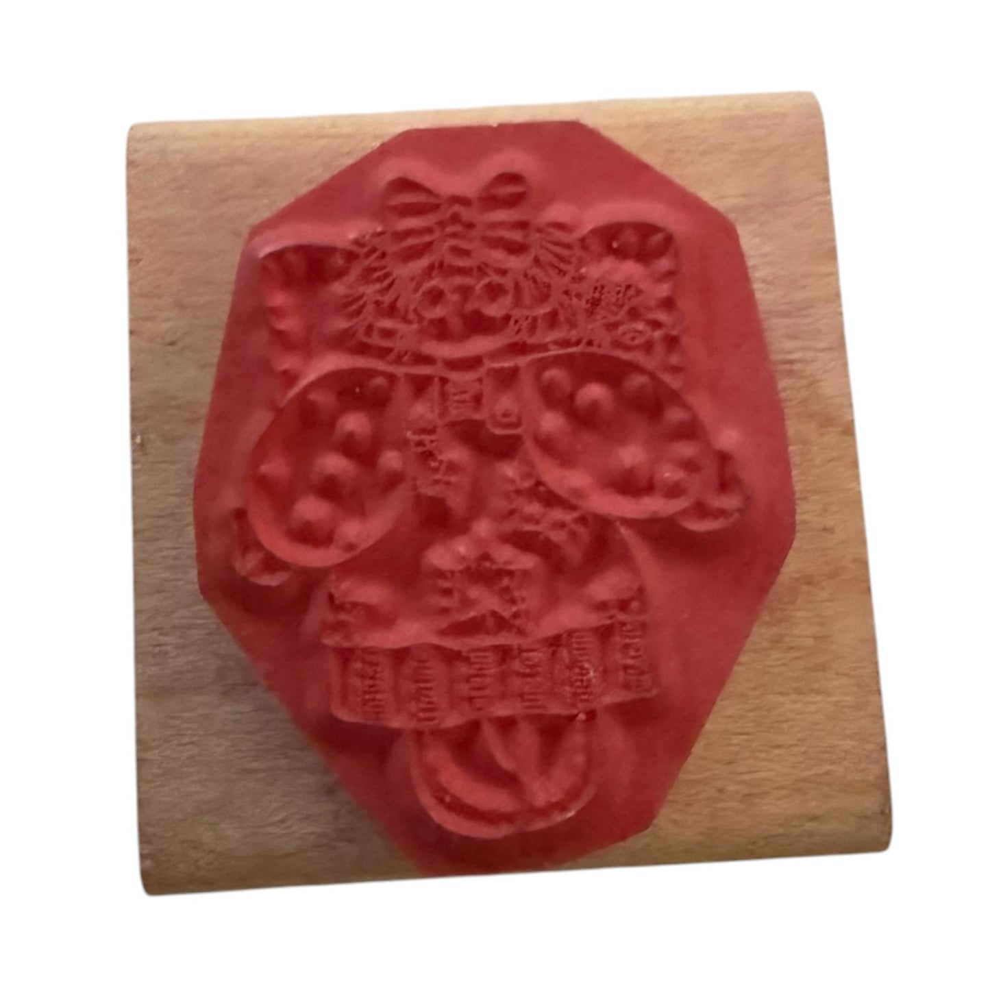 A red rubber stamp with a doll character design, mounted on a light-colored wooden block against a plain white background.