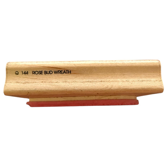 A wooden stamp handle with a red rubber stamp base, featuring the text 'Q 144 ROSE BUD WREATH' printed in black on the side, set against a plain white background.