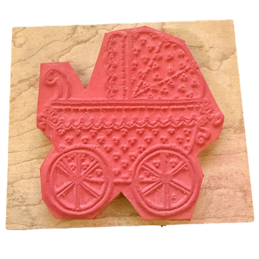 A pinkish-red rubber stamp shaped like a vintage baby carriage, mounted on a square beige wooden block against a white background.