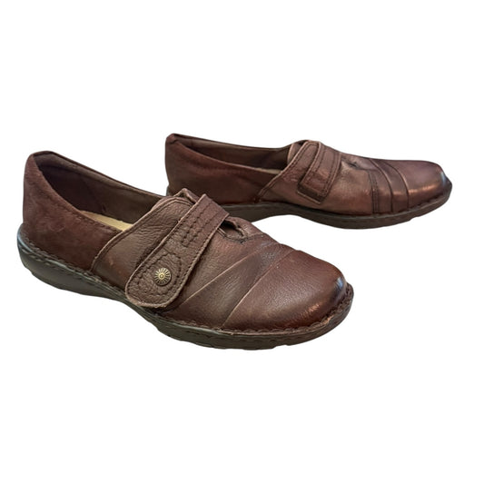 A pair of women's brown leather with strap closures and a decorative metal snap, shown on a plain white background.