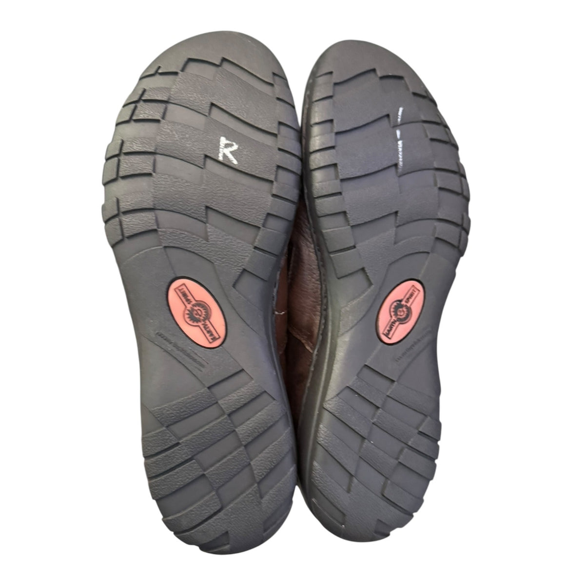 A pair of shoes shown from the sole side, featuring a dark gray textured rubber tread with a pink circular logo patch and a white letter 'R' on the right sole.