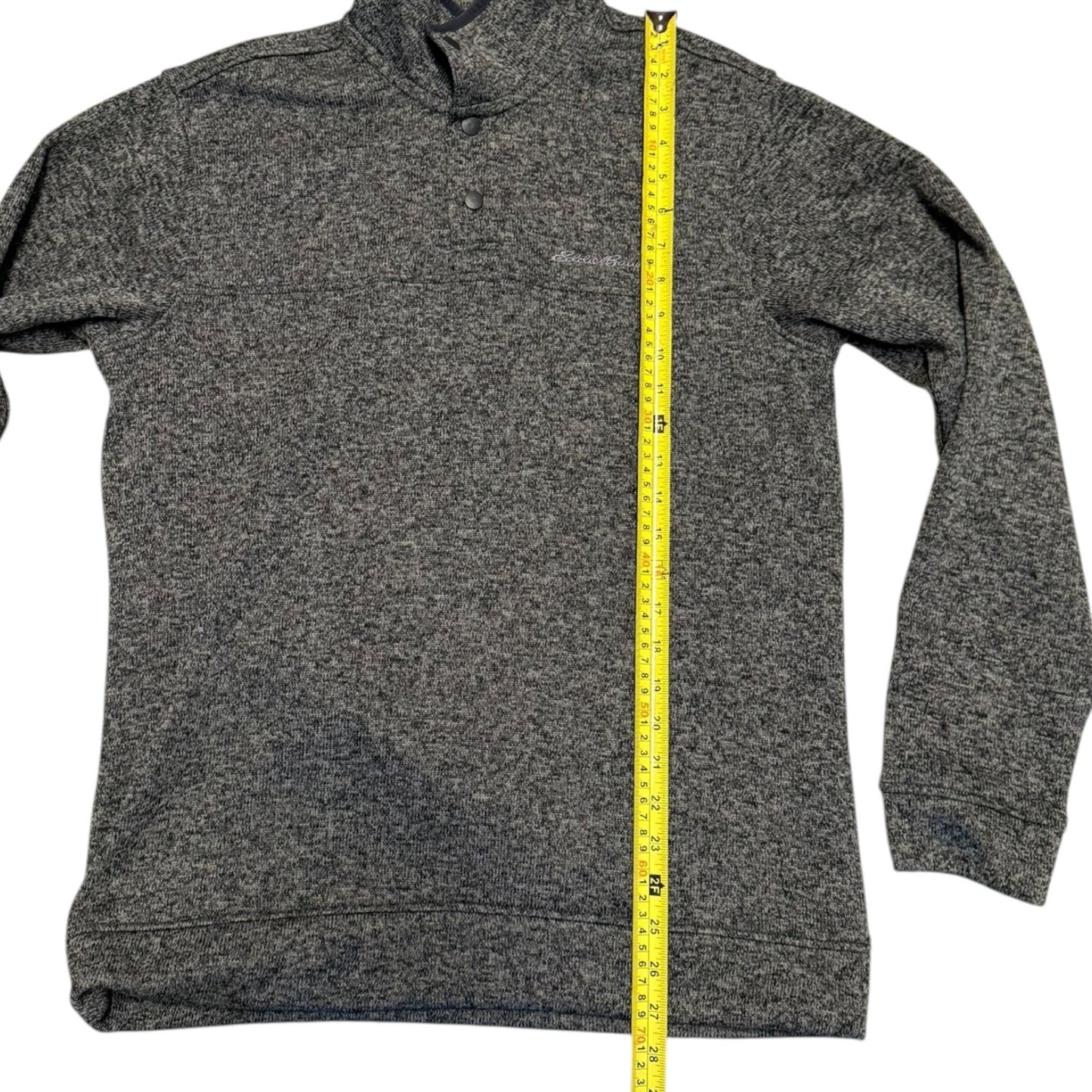 A gray long-sleeve quarter-zip pullover sweater shown flat against a white background, with a yellow tape measure standing vertically along the center to indicate size.
