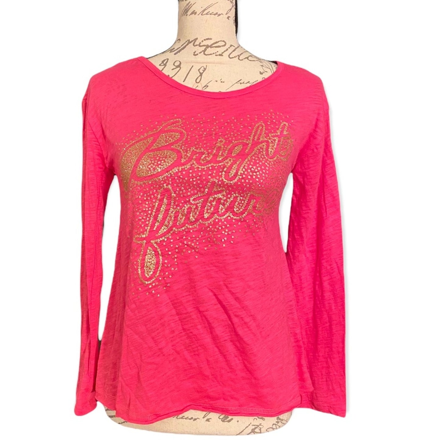 A bright pink long-sleeve t-shirt with a glittery gold graphic reading 'Bright Future' on the front, displayed on a vintage-style dress form mannequin against a white background.